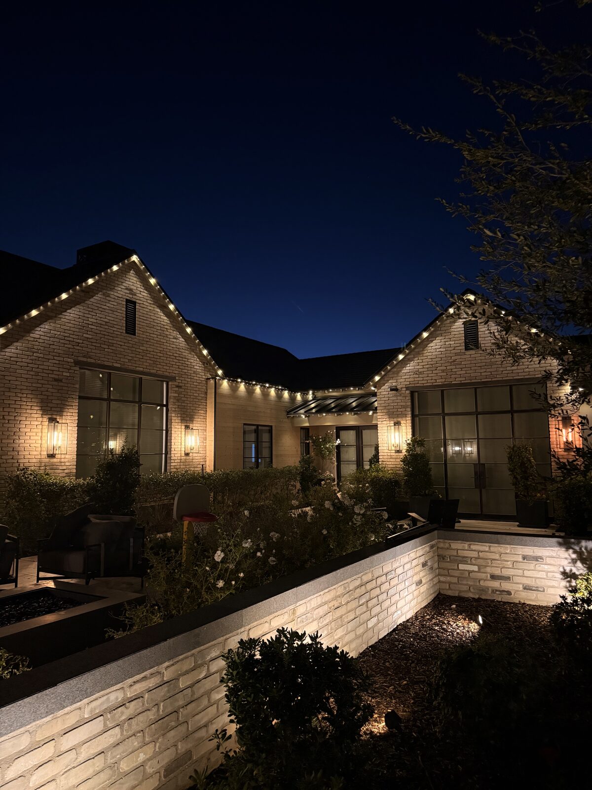 Two-story white brick home with warm white permanent lighting along the roofline