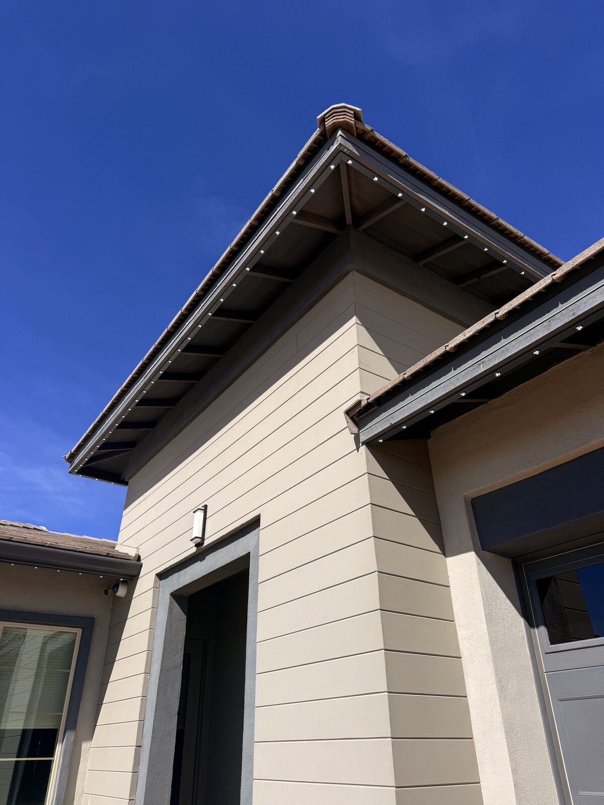 Daytime view of warm white permanent lighting fixtures on blue trim home